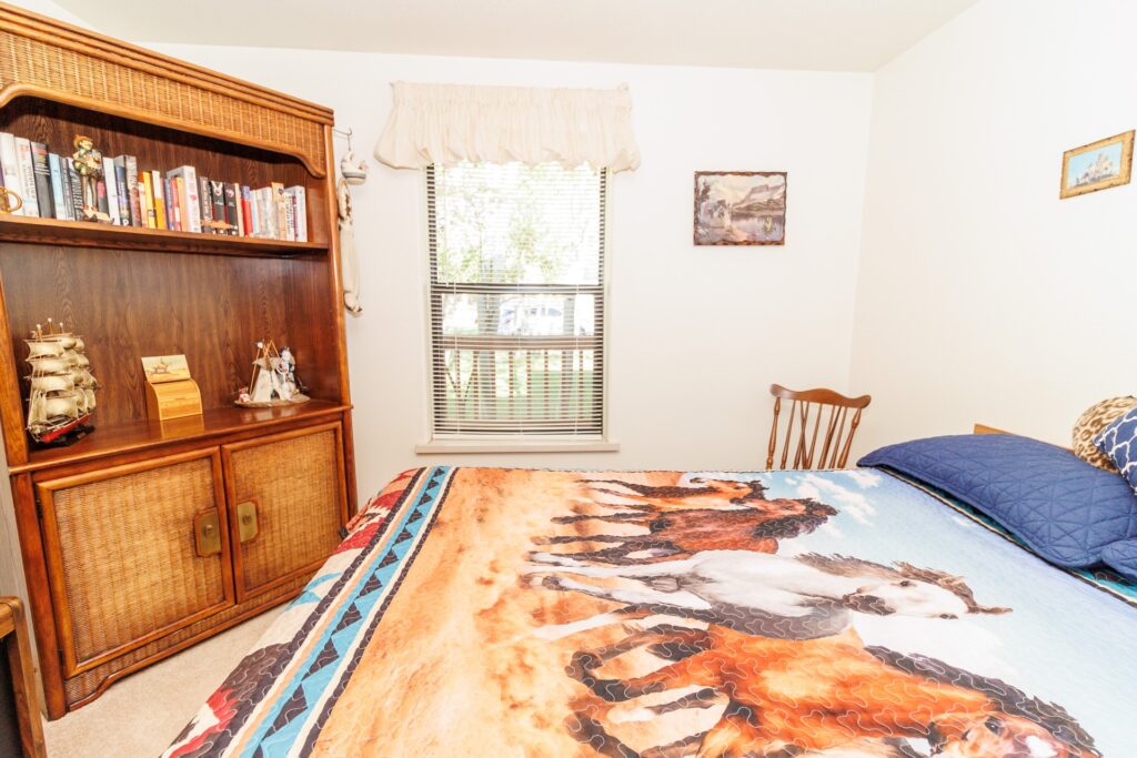 Cozy bedroom featuring a horse-themed quilt, a wooden bookshelf with books, and a sunny window, highlighting a warm and inviting atmosphere.