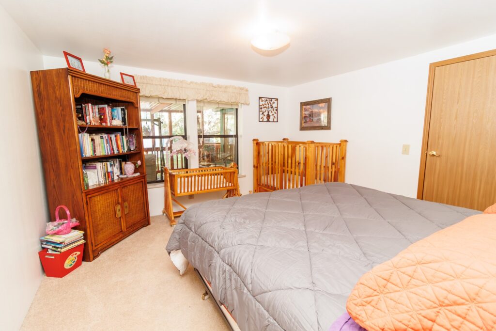 Cozy bedroom featuring a large bed, wooden bookshelf, and a crib, with windows allowing natural light. Ideal for family or guest accommodations.