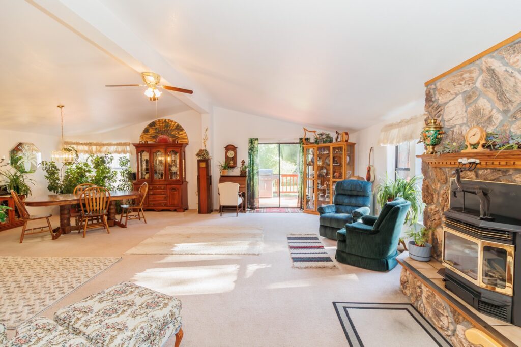 Bright and spacious living room featuring a large dining table, green recliners, stone fireplace, and sliding door to an outdoor deck.