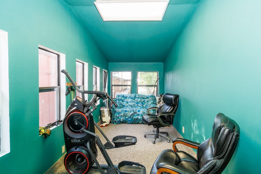 A bright turquoise room featuring an exercise machine, two black chairs, and a floral-patterned couch, ideal for workouts and relaxation.