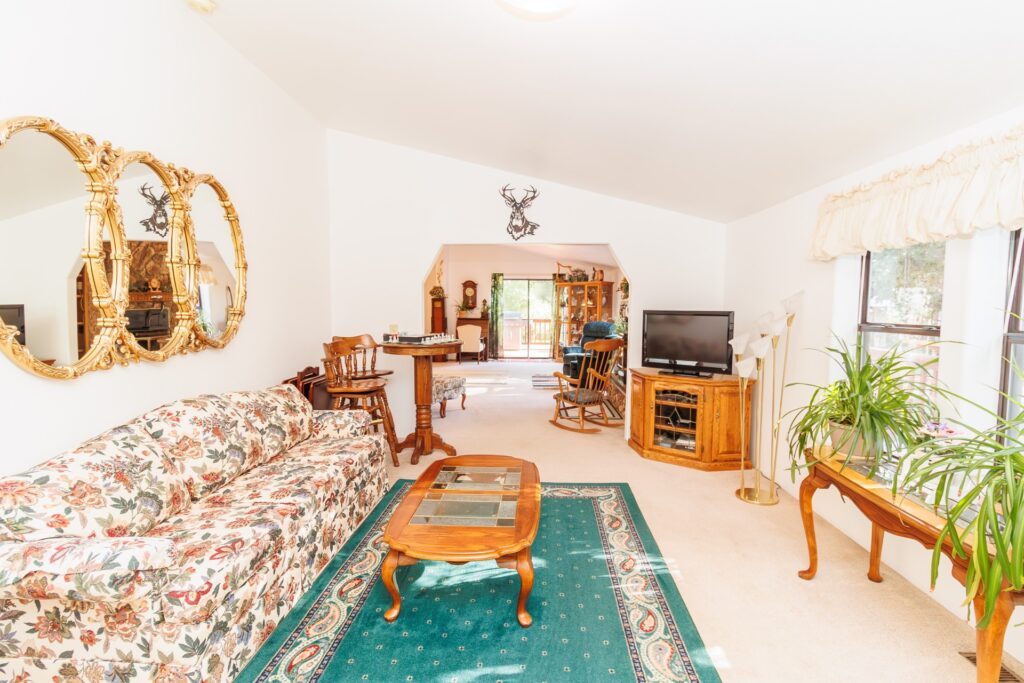 Cozy living room featuring floral-patterned couch, wooden furniture, and mirrors. Natural light illuminates the space, showcasing a welcoming atmosphere.