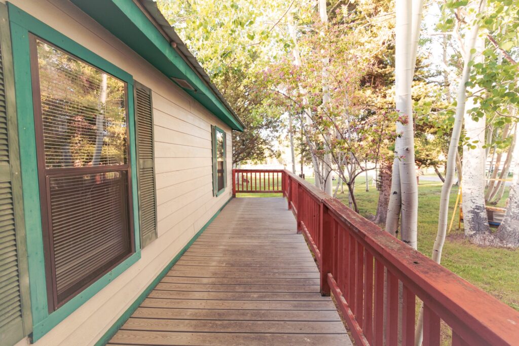 Wooden walkway leading to a house with green trim, bordered by trees and greenery, creating a peaceful, natural setting.