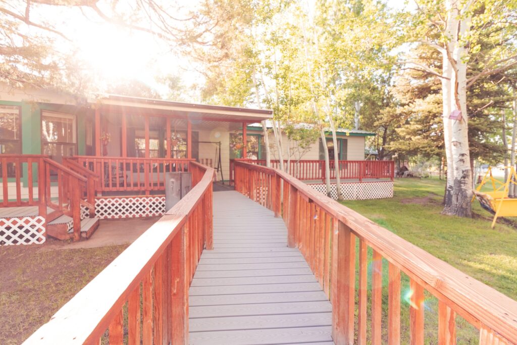 Wooden walkway leading to a cozy cabin, surrounded by trees and green grass, perfect for outdoor relaxation or gatherings.